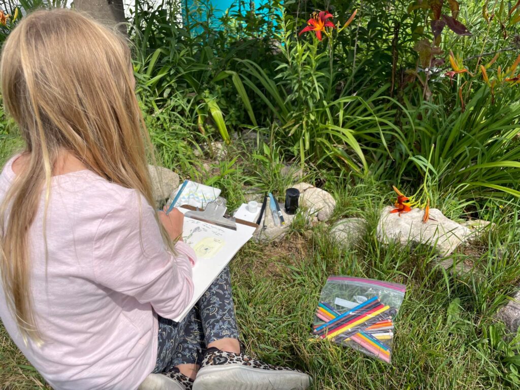 Camper sketching a flower in the pollinator garden. 